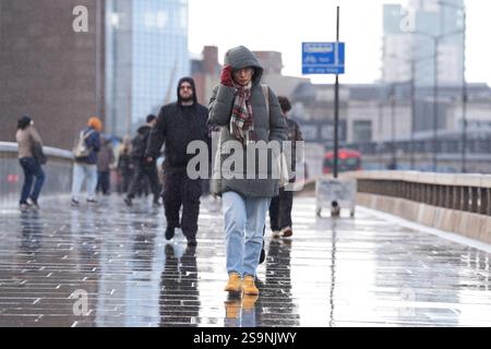Les gens s'abritent de la pluie en traversant London Bridge dans le centre de Londres. Les tempêtes provoquent des inondations et des perturbations accrues dans les transports à travers de grandes parties de l'Angleterre et du pays de Galles. Date de la photo : lundi 27 janvier 2025. Banque D'Images