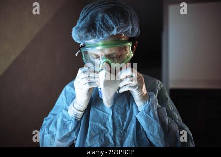 Un travailleur médical ajuste un masque de protection dans un cadre de laboratoire, se préparant au travail Banque D'Images