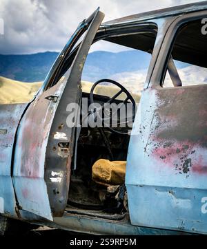 Un camion vintage abandonné avec une porte ouverte, révélant un intérieur et un volant usés. L'extérieur du chariot présente des signes de rouille et d'altération des intempéries, s Banque D'Images