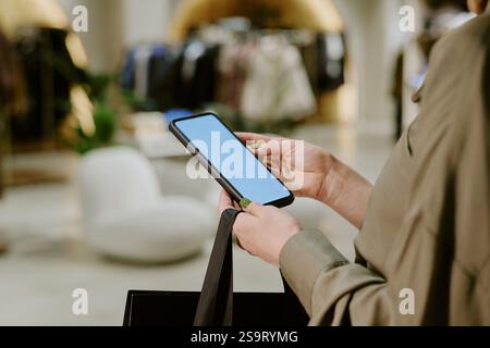 Smartphone noir moyen gros plan avec écran blanc dans des mains féminines élégantes méconnaissables Banque D'Images