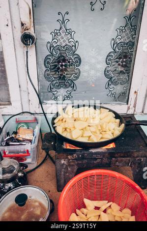 Pommes de terre frites dans une poêle à frire, cuisine dans le pauvre camp de réfugiés mendiant Banque D'Images