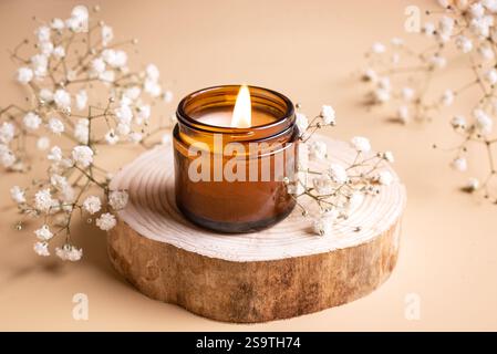Bougie à arôme de cire de soja brûlante et fleurs blanches de gypsophila en gros plan. Bougie de massage parfumée, concept de relaxation et de décoration intérieure. Banque D'Images