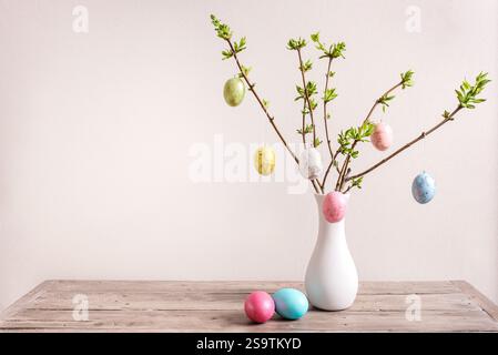 Bouquet de Pâques avec des œufs de Pâques peints et des branches de printemps dans un vase blanc, fond neutre, design esthétique minimal avec espace de copie. Joyeuses Pâques Banque D'Images