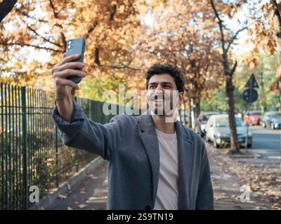 Gros plan portrait d'un jeune homme souriant du moyen-Orient prenant selfie avec téléphone sur une belle journée d'automne. Banque D'Images