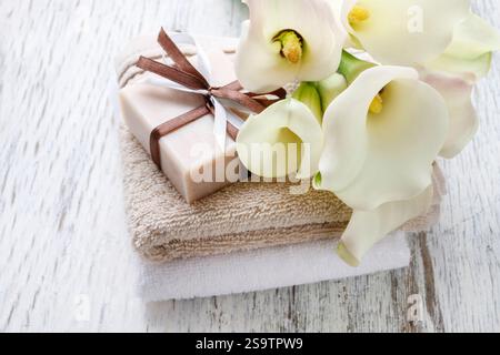 Barre de savon naturel fait à la main, serviettes et bouquet de fleurs de calla blanc sur table en bois rustique. Banque D'Images