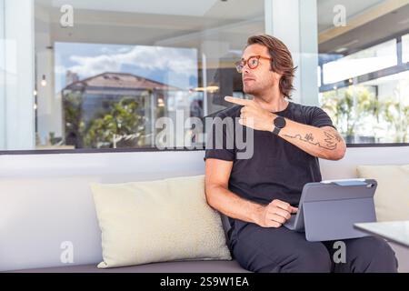 Un homme d'affaires hipster avec un tatouage sur son bras pointe vers la gauche, photo de l'espace de copie Banque D'Images