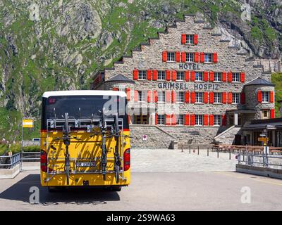 Grimselpass, Suisse - 8 août 2024 : L'hôtel Grimsel Hospiz est un hôtel historique situé dans les Alpes suisses. Autobus postal jaune transportant des bicyclettes i Banque D'Images