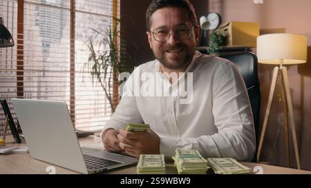Heureux souriant caucasien chef de chef de chef de travail homme vendeur homme Guy tenant pile de profit d'argent dans le bureau pdg entrepreneur d'homme d'affaires sentent des dollars Banque D'Images