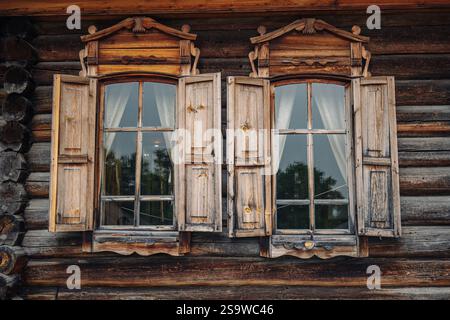 Fenêtres en bois vintage ouvertes avec des architraves sculptées et des volets légèrement ouverts sur une cabane en rondins russe traditionnelle Banque D'Images