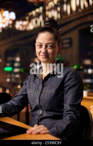 Portrait d'une bibliothécaire confiante travaillant sur son ordinateur portable dans une bibliothèque scolaire, axée sur la fourniture de ressources académiques et de conseils. Évaluation des supports d'apprentissage dans la base de données. Banque D'Images