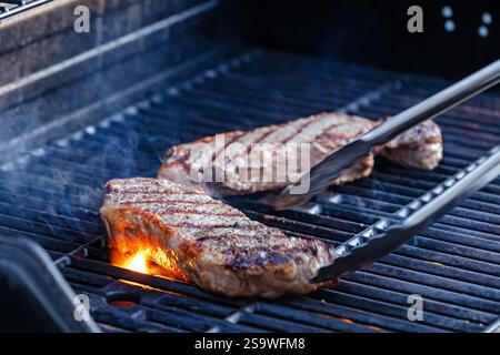 Vue rapprochée de deux steaks juteux grésillant sur le grill extérieur chaud Banque D'Images