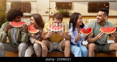 Joyeux et divers jeunes amis mangeant de la pastèque fraîche et juteuse, assis près d'un camping-car lors d'un voyage d'automne à la campagne Banque D'Images