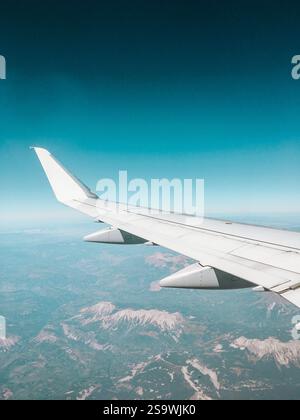 Superbe photographie d'une aile d'avion survolant le paysage montagneux de la Grèce, capturant les sommets et les vallées spectaculaires ci-dessous. Banque D'Images