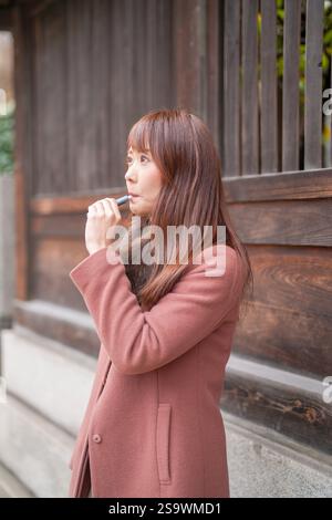A côté des bâtiments historiques au Japon. Une japonaise aux cheveux longs dans la trentaine regarde la ville en fumant des cigarettes électroniques. Banque D'Images