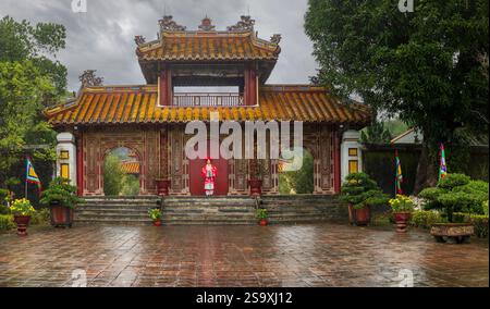 Vietnam, Hue. Jeune femme vietnamienne posant dans sa robe de célébration du nouvel an appelée Ao Dai devant l'entrée du temple traditionnel et ancien. (M.) Banque D'Images