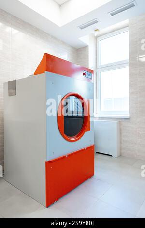 Buanderie moderne avec une grande laveuse industrielle au design orange et gris dans un environnement bien éclairé Banque D'Images