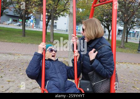 Deux femmes seniors bénéficiant d'ride sur des balançoires dans le parc, des personnes âgées, la retraite d'amis Banque D'Images