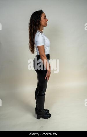 Photo studio d'une jeune femme aux longs cheveux bruns, posant latéralement en t-shirt blanc et legging noir Banque D'Images