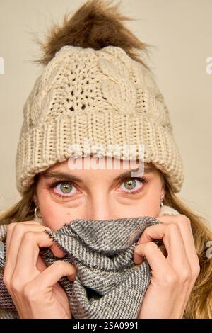 Gros plan d'une femme couvrant son visage avec une écharpe chaude tout en portant un bonnet beanie tricoté avec un pompon, cherchant à se protéger du froid Banque D'Images