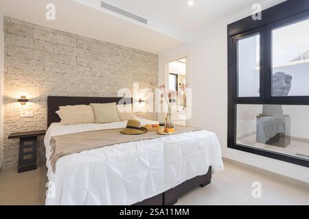 Une chambre lumineuse avec un mur d'accent en pierre, un lit soigneusement fait avec des oreillers, et un plateau de petit déjeuner avec des accents décoratifs. Banque D'Images