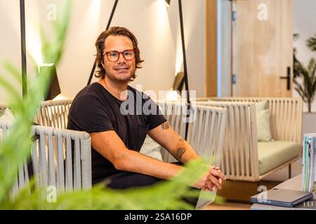 Un homme hipster dans une chemise noire portant des lunettes est assis dans une chaise, photo avec espace de copie. Banque D'Images