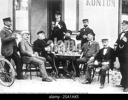 Le mode de vie des hommes au début du XXe siècle. Un groupe d'hommes sont assis à une table dehors en train de déguster un verre de bière. Ils sont tous les trois généralement bien habillés et chapeaux sont sur. Des bouteilles de bière sont vues sur la table. Suède 1800-1900 BV67-5 Banque D'Images
