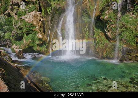 Un arc-en-ciel s'étend sur une cascade qui se jette dans l'eau turquoise claire, entourée de rochers, Topoljski Buk Kovacic Dalmatia Croatie Banque D'Images