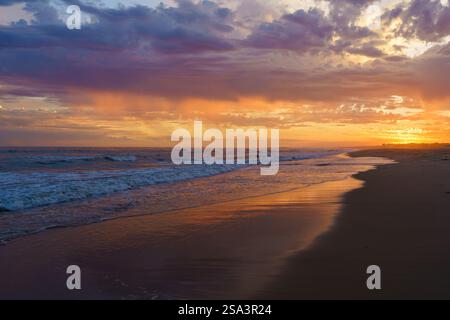 Les couleurs éclatantes du coucher de soleil se reflètent sur le rivage tandis que les vagues roulent doucement. Banque D'Images