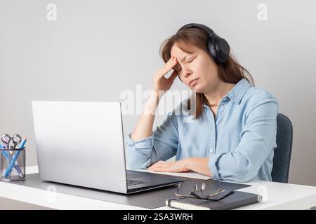 Une femme freelance surchargée de travail est fatiguée et stressée derrière son ordinateur portable. Problème d'épuisement et d'épuisement du travail à distance. La femme lutte avec fatigu Banque D'Images
