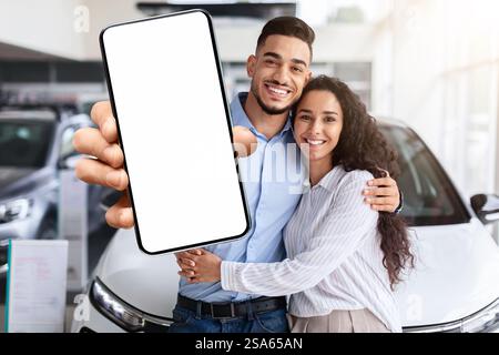 Famille musulmane aimant montrant un smartphone avec écran vierge, achetant la voiture Banque D'Images