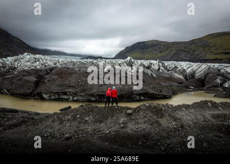 Vue aérienne par drone du paysage glaciaire islandais de Svinafellsjokull 1 en Islande avec deux personnes avec des vestes rouges et de la glace bleue accidentée et des montagnes Banque D'Images