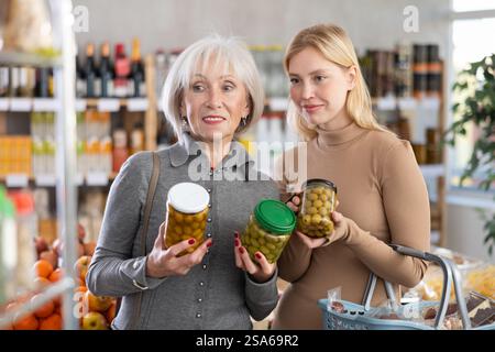 Une mère âgée avec sa fille adulte choisit des olives vertes en conserve pour acheter dans la section du magasin du rayon épicerie Banque D'Images