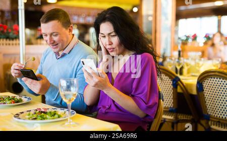 Couple biracial adulte utilisant un téléphone pendant le déjeuner au restaurant Banque D'Images