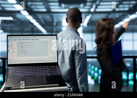 Ordinateur portable dans un centre de données avec des programmeurs en arrière-plan flou utilisant des modèles d'apprentissage automatique. Ordinateur portable utilisé par les experts INFORMATIQUES travaillant en équipe qui utilisent un ordinateur portable pour répondre aux besoins en infrastructure, gros plan Banque D'Images