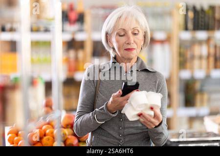 Femme âgée scannant le code qr pour le yaourt Banque D'Images