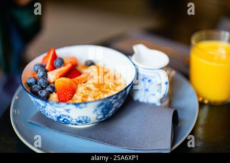 Un bol de flocons d'avoine crémeux garni de fraises fraîches, de bleuets et d'une pincée de cannelle, servi avec du lait et un verre de jus d'orange pour Banque D'Images