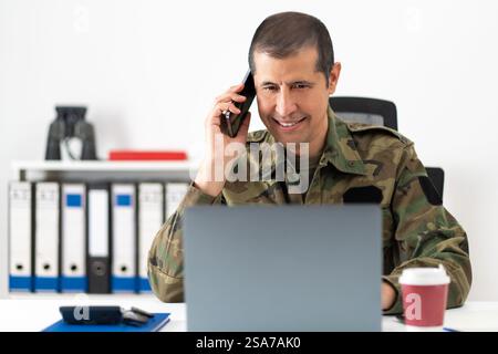 Beau soldat américain derrière son ordinateur parlant au téléphone au bureau Banque D'Images