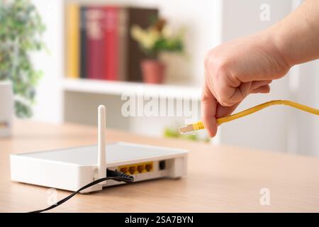 Gros plan d'une main d'homme branchant le câble ethernet au routeur sur un bureau à la maison Banque D'Images