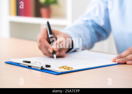 Épouse signant le document de divorce avec des anneaux de mariage au-dessus au bureau Banque D'Images