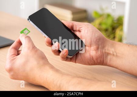 Gros plan des mains d'un homme mettant la carte sim sur le téléphone sur une table Banque D'Images
