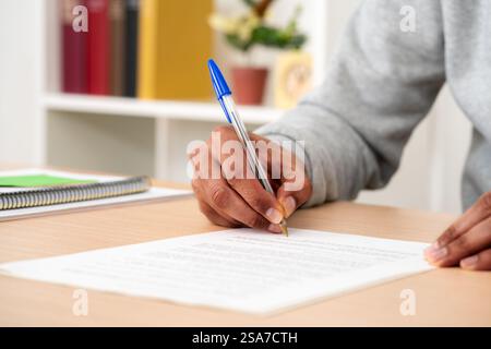 Gros plan sur le document de signature des mains de l'homme noir sur un bureau à la maison Banque D'Images