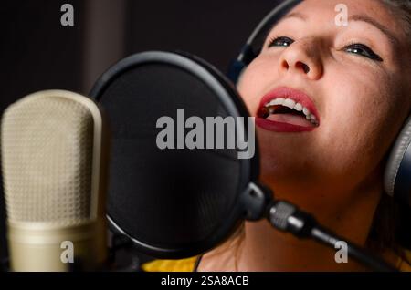 Jeune chanteuse portant des écouteurs enregistrant une nouvelle chanson dans un studio professionnel Banque D'Images