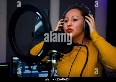 Jeune femme enregistrant une piste audio dans un studio professionnel, portant des écouteurs et chantant dans le microphone Banque D'Images