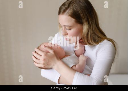 L'enfant pleure dans les bras de sa mère, une mère fatiguée regarde son nouveau-né avec amour, la calme. Concept de maternité, congé de maternité, problème de sommeil Banque D'Images