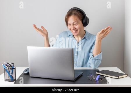 Femme professionnelle indépendante joyeuse portant de gros écouteurs parlant sur la réunion de chat en ligne à l'aide d'un ordinateur portable, parlant sur l'appel de vidéo conférence, souriant, Banque D'Images