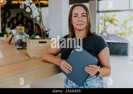 Une femme tient une tablette dans sa main et sourit. Elle est debout devant une plante en pot et un vase. Banque D'Images
