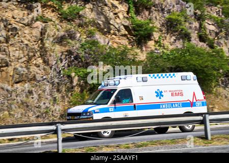 Philipsburg, Saint-Martin, Caraïbes - 3 janvier 2025 : ambulance à Philipsburg, Saint-Martin. Une ambulance de l'EMS en action sur une route près d'une paroi rocheuse *** Rettungswagen à Philipsburg, Sint Maarten. Ein Krankenwagen der Maarten EMS im Einsatz auf einer Straße nahe einer Felswand Banque D'Images