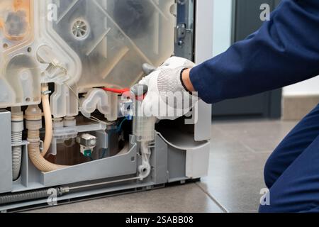 Photo d'un jeune homme utilisant un tournevis pendant la réparation d'un lave-vaisselle dans une maison Banque D'Images