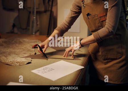 Individuel debout à l'établi en studio coupant le motif de tissu avec précision, se concentrant intensément sur la tâche. Ciseaux et morceaux de papier éparpillés sur la surface de travail Banque D'Images