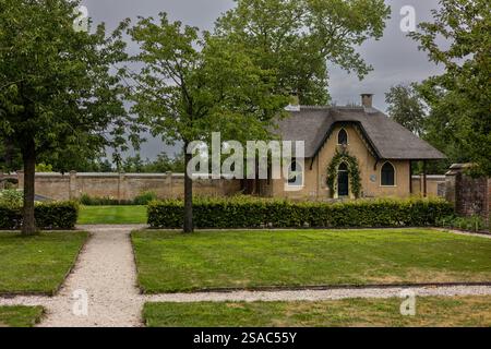 Une charmante maison en briques avec un toit de chaume, des fenêtres cintrées, et une porte verte couverte de plantes grimpantes. La maison se trouve dans un jardin luxuriant, avec un cobb Banque D'Images